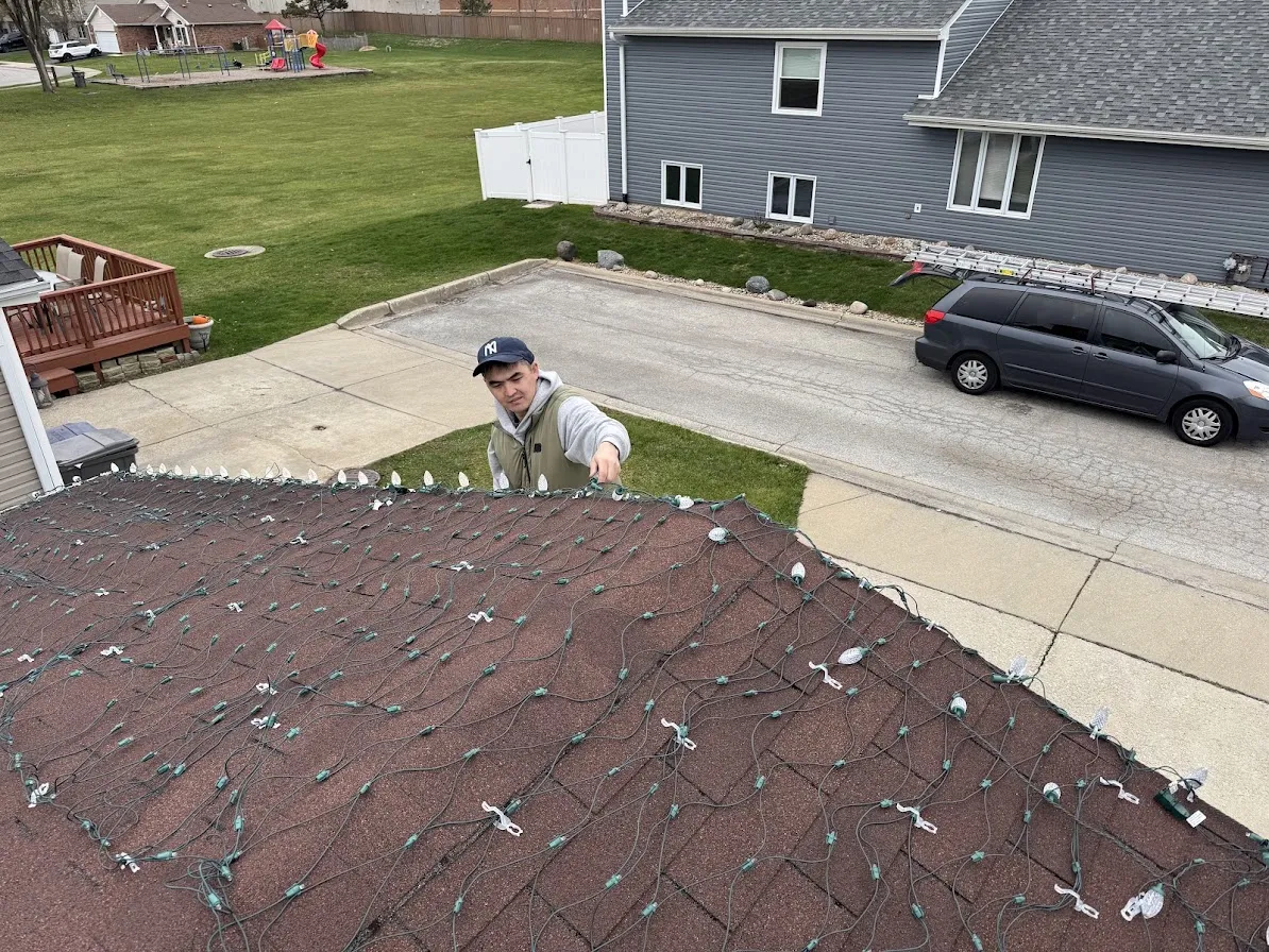 Holiday light installer securing string lights along a roof edge