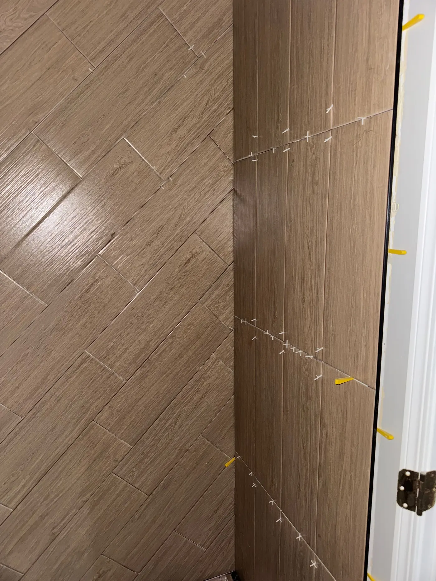 Wood-look tile installation in progress with spacers visible at the wall transition
