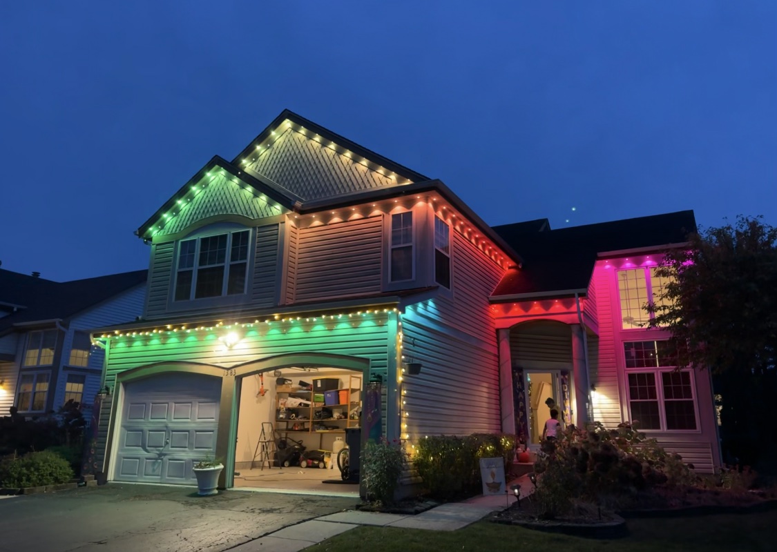 Two-story house at dusk with green, warm white, and red permanent roofline lighting