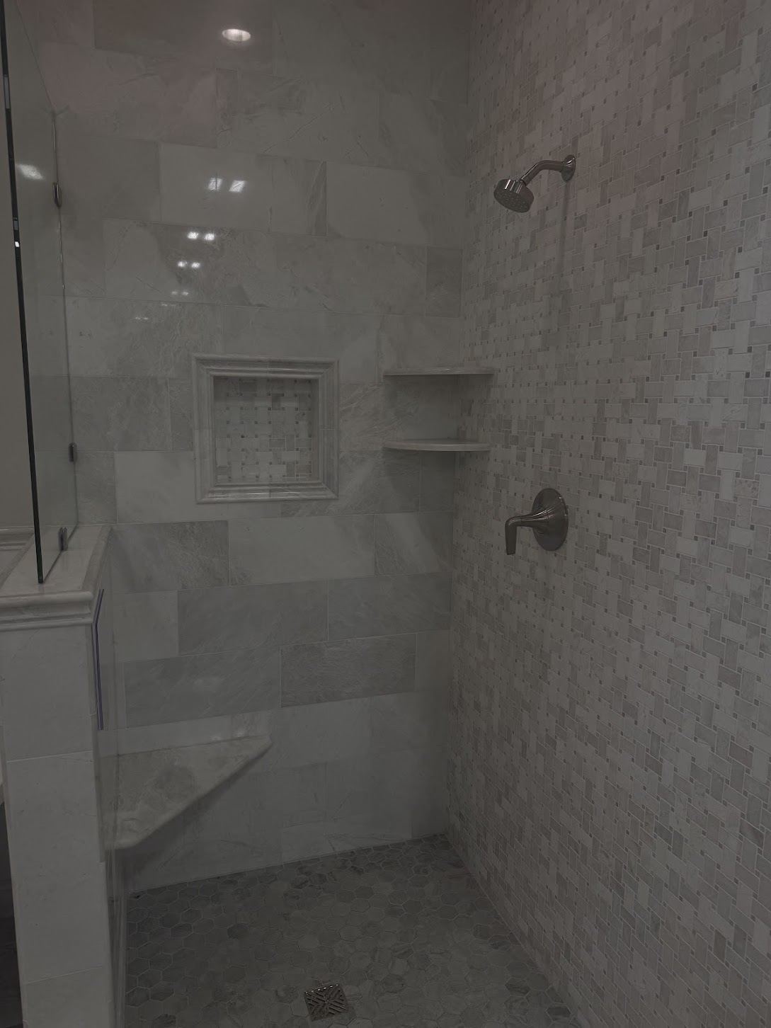 Marble-look tiled shower with a built-in bench